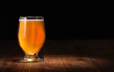 Siyah arka planda köpüksüz bira ve ahşap bir masa.