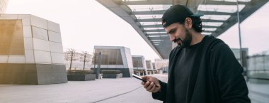 Issız bir şehirde elinde telefon olan bir adam. Genç bir adam, boş bir metropolde, üzerinde insanlar olmayan akıllı bir telefona bakıyor.