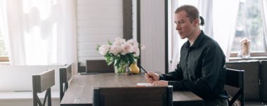 Genç bir adam masadaki bir deftere yazar. Gazeteci, yazar notlar alır, işyerindeki yazılar üzerinde çalışır.