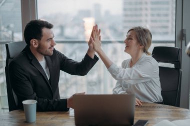 İş dünyasında takım çalışması. Ortaklar masadaki başarıya sevinir, birbirlerine beş dakika verirler. Erkek ve kadın ortaklar, iş arkadaşları iş meselelerini masada ve dizüstü bilgisayarda tartışır