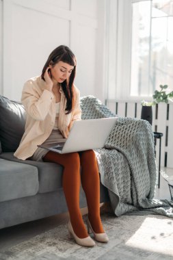 Genç bir kadın dizüstü bilgisayarda çalışıyor, güneşli bir günde modern ve parlak bir ofiste internetten iletişim kuruyor. Güzel esmer kız kanepede oturur, çalışır, video konferansı yönetir, online ders verir.