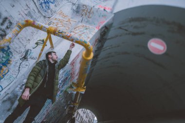 Şehir modern mekanında ceketli genç bir adam, açık havada grafiti yapıyor. Yakışıklı bir adam Moskova 'daki sanat eserlerinin duvarlarında poz veriyor.