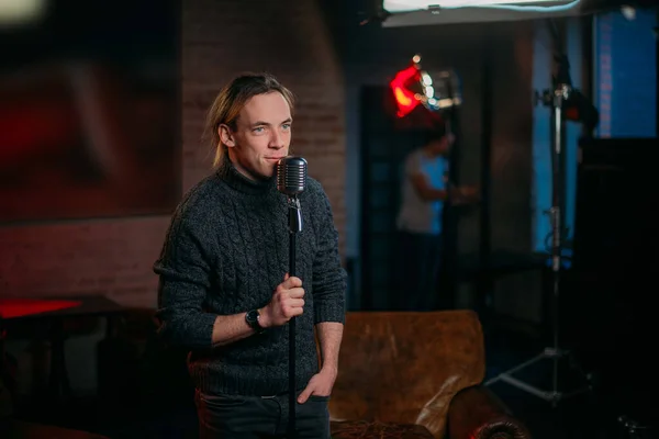 Shooting a stand-up show. Stand-up comedian on stage at the microphone. A young man, an author of jokes and comedy texts, stands on a stage in a studio during the filming of a show.