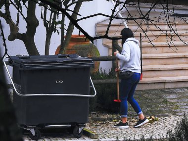 Young worker clearing the street of leaves near a container