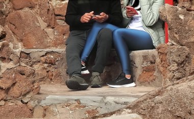 Birbirini seven bir çift kayalıklarda oturmuş cep telefonlarına danışıyor.