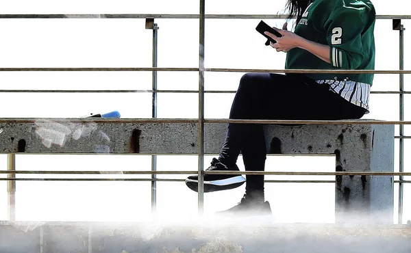 The young woman in the green jacket consulting her cell phone on a bench