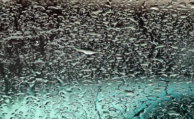 Yağmurun altında ön planda sıçramalar olan bir arabanın ön camı.