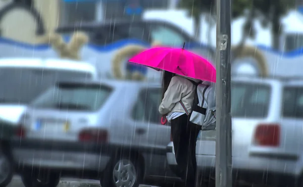 Woman with fuchsia umbrella in the rain waiting for the bus