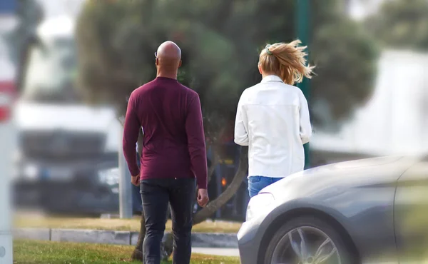 A bald man with a blonde walking through a parking lot