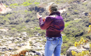 Mor ceketli kadın cep telefonuyla fotoğraf çekiyor.