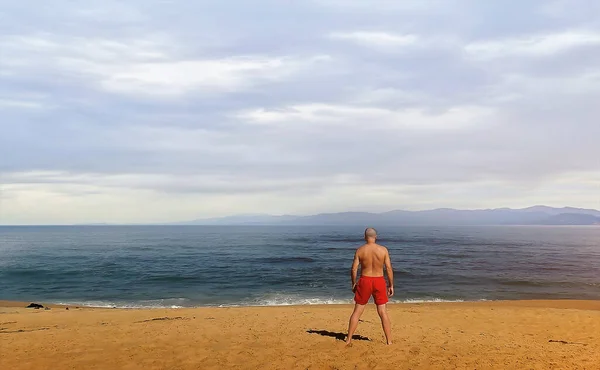 An adult man in briefs alone on the beach