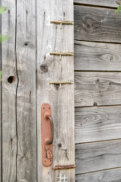 Rostige Türklinke und drei Klinken an einer Holzscheune oder Toilettentür, auf dem Land. — Stockfoto