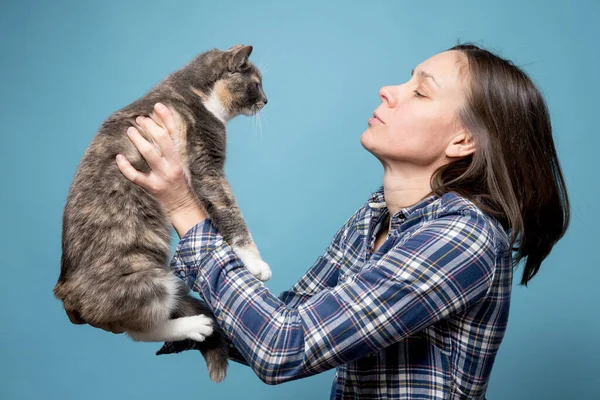 Kvinna i skjorta håller sin förtjusande katt i händerna och tittar uppmärksamt på henne. Begreppet lek och skötsel av husdjur. — Stockfoto