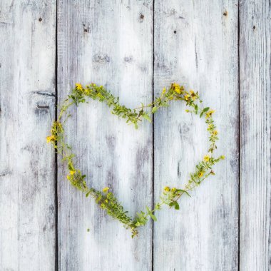 Kalp sembolü, ahşap bir masada sarı çiçekli tıbbi hiperikum ile kaplıydı. Sağlıklı kurutulmuş bitki çayı. Üst görünüm.