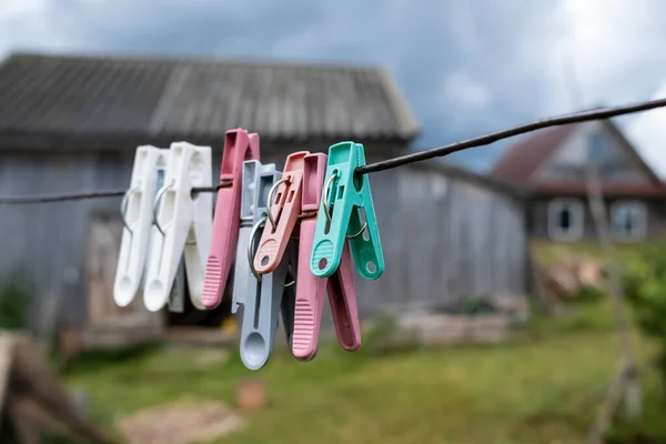 Plastic clothespins hang on clotheslines, in a rustic courtyard, against the backdrop of a wooden barn and the sky. — Stock Photo, Image