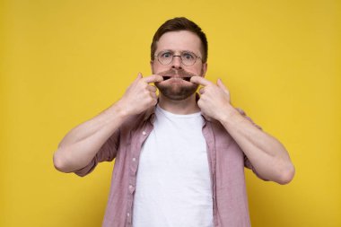 Gözlüklü tuhaf adam korkunç bir şekilde yüzünü buruşturdu. Parmaklarını ağzına soktu ve kameraya baktı.. 