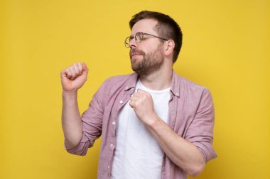 Gözlüklü beyaz bir adam en sevdiği müziği dinliyor ve dans ediyor. Gözlerini kapatıyor ve sesten hoşlanıyor. Sarı arkaplan.