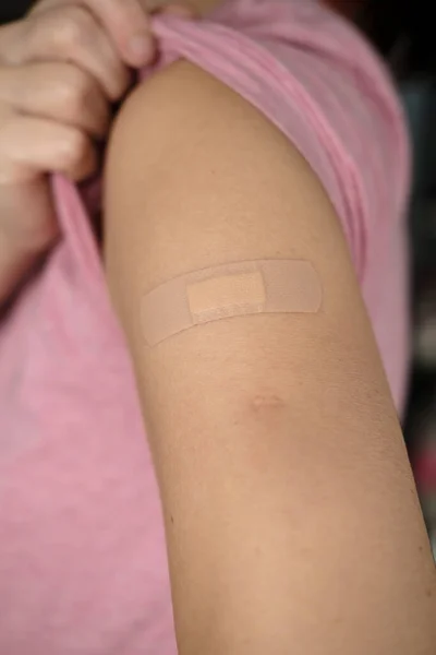 Main après avoir été vacciné contre le covide-19. Femme lève la manche d'un t-shirt et montre son épaule avec un bandage après la vaccination. — Photo