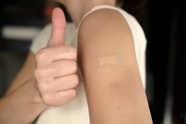 Close-up van een vrouwelijke schouder met een verband na een covid-19 vaccinatie en een gebaar van goedkeuring, duim omhoog. Gezondheidsconcept. — Stockfoto