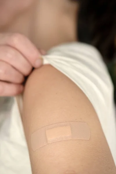 Gros plan d'une main après avoir été vaccinée contre la covide-19. Femme en t-shirt blanc montre son épaule avec un bandage après la vaccination. — Photo