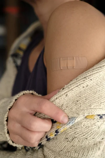 Primer plano de una mano femenina con un vendaje después de la vacuna covid-19. La mujer se ha quitado el suéter del hombro y muestra la vacunación.. —  Fotos de Stock