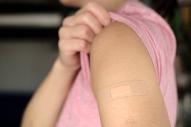 Covid-19 'a karşı aşı olduktan sonra. Kadın bir tişörtün kolunu kaldırır ve aşıdan sonra omzunu bandajla gösterir..