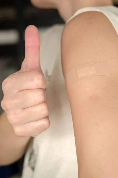 Close-up van een vrouwelijke schouder met een verband na een covid-19 vaccinatie en een gebaar van goedkeuring, duim omhoog. Gezondheidsconcept. — Stockfoto