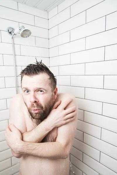 El hombre desnudo se abraza en la ducha, se congela y tiembla, porque de repente el agua caliente desapareció y solo quedó agua fría. — Foto de Stock
