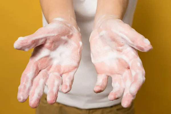 La mujer muestra sus manos en jabón, sobre un fondo amarillo. Concepto para una manera efectiva de prevenir la propagación de infecciones. Primer plano. — Foto de Stock