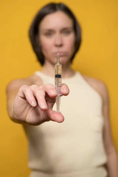 Серьёзная белая женщина держит в руке шприц с жидкостью. Концепция вакцинации от наркомании или ковида-19. — стоковое фото