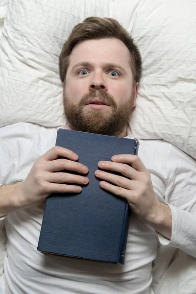 Stunned man lies in bed clutching the book he has finished to chest and looks up enthusiastically. Top view. — Stock Photo, Image