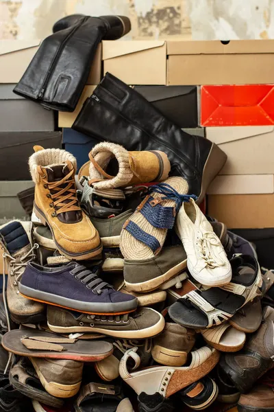 오래 되고 다양 한 신발들이 쌓여 있는 신발 상자들. 낡아 빠진 낡은 벽의 배경에 고립되어 있는 모습. — 스톡 사진
