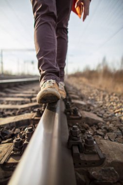Sarı çizmeli erkek ayakları arka planda bulanık bir şekilde demiryolu rayları boyunca güvenle yürür. Tehlikeli bir yürüyüş..