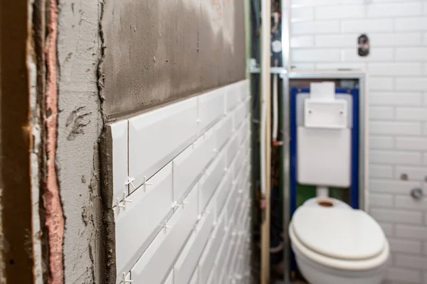 Białe płytki przyklejane są do specjalnej zaprawy, w łazience, na tle muszli klozetowej. Proces dekoracji ścian. Naprawy domów. — Zdjęcie stockowe