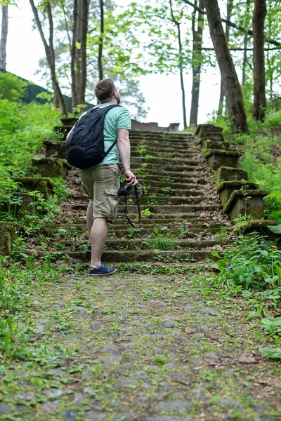 Tourist with a camera in his hands and a city backpack stands in front of the ancient stone steps and enjoys beautiful views. — Stock Photo, Image