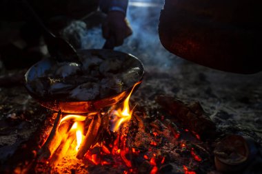 Taze tutulan balık parçaları kamp ateşinin üzerinde, gece geç saatlerde bir kamp alanında tavada kızartılıyor. Hobi ve yaşam tarzı. 