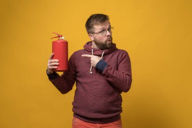 Gözlüklü adam elinde bir yangın söndürücü tutuyor ve işaret parmağıyla sürekli ona doğrultuyor.. 