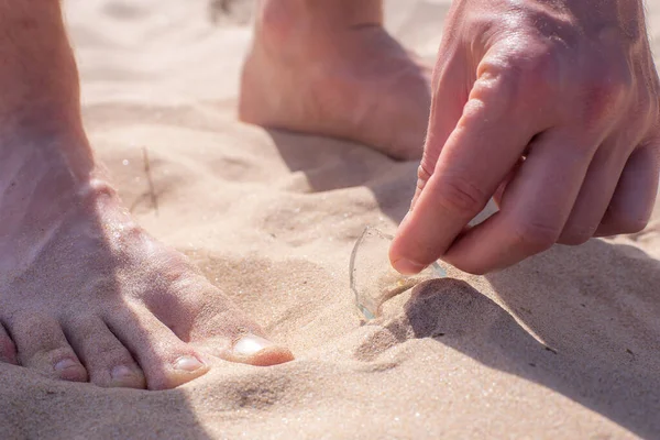 El hombre descalzo caminaba por la playa y encontró un fragmento de vidrio roto de una botella que yacía peligrosamente en la arena. — Foto de Stock