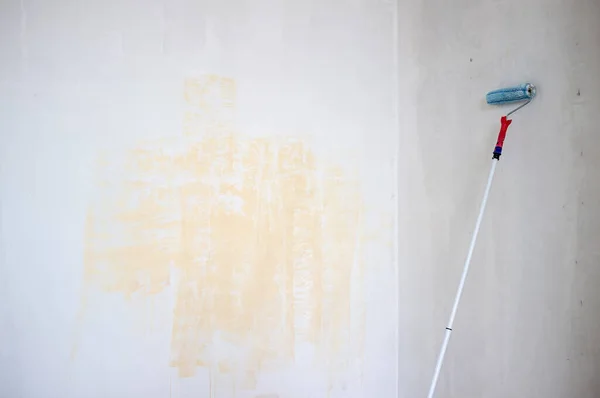 A velha parede está pronta para ser pintada com um rolo em um pau de madeira. Renovação da casa. Espaço de cópia. — Fotografia de Stock