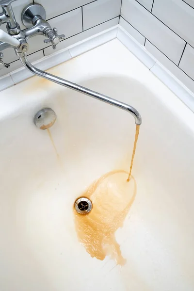 A água ferrugenta flui da torneira para uma banheira branca. O problema são os tubos antigos que precisam ser substituídos. — Fotografia de Stock