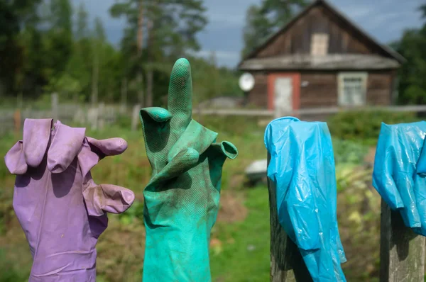 De vieux gants en caoutchouc sale de différentes couleurs sont séchés sur la clôture, dans la cour du village. Gros plan. — Photo