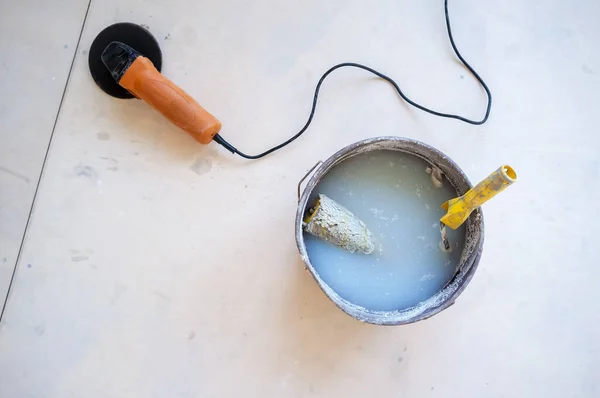 Farbwalze in einem Eimer Wasser, neben einem Elektroschleifer. Haussanierung. Kopierraum. — Stockfoto