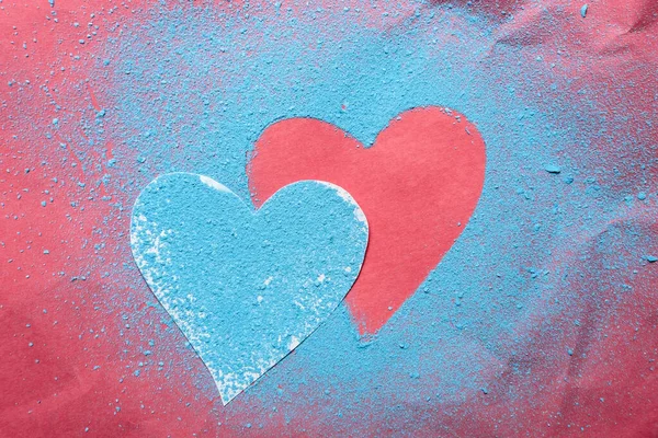 День Святого Валентина. Два сердца являются символом любви, одно посыпанное ярко-голубым порошком, а другое на красном текстурированном фоне. — стоковое фото