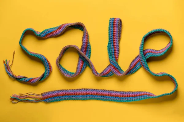 Надпись ПРОДАЖА выполнена с разноцветным трикотажным шарфом на желтом фоне. Концепция новогодних скидок и покупок. Лицензионные Стоковые Фото