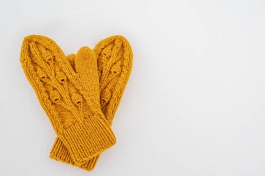 Knitted yellow mittens lie on pure white snow on a cloudy winter day. Copy space. Top view. 