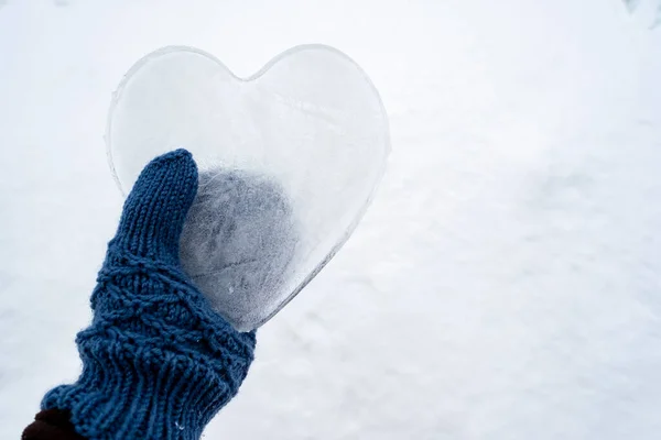 Hati - simbol cinta, yang terbuat dari es, dipegang oleh tangan dengan sarung tangan rajutan biru hangat. Hari Valentine. Konsep romantis. Salin ruang. — Stok Foto