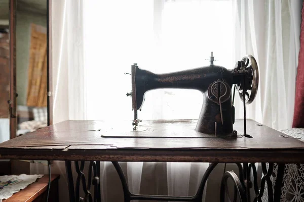 Vintage mechanical sewing machine with a table stands by a window in a rustic house. — стоковое фото