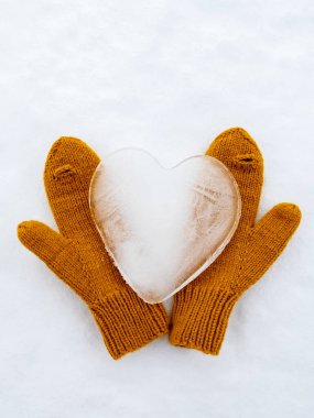 Valentines Day. Heart-symbol of love, made of ice, on warm yellow knitted mittens, on the snow. Romantic concept. Top view. 