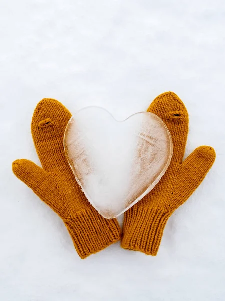Hari Valentine. Simbol hati cinta, terbuat dari es, pada sarung tangan kuning hangat rajutan, pada salju. Konsep romantis. Tampilan atas. — Stok Foto