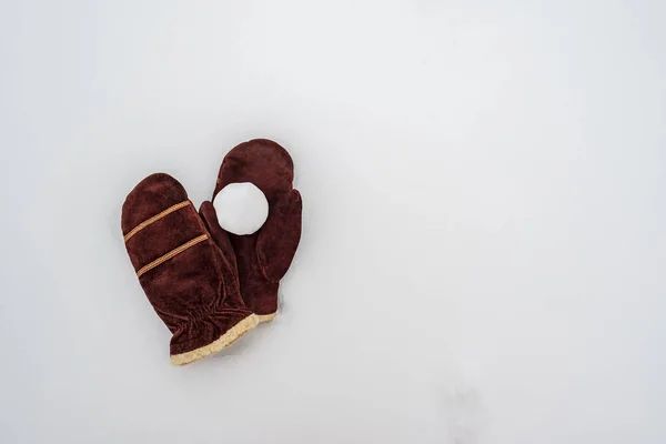 Snowball on brown suede warm mittens, in the snow. Winter active games and entertainment. Copy space. — Stock Photo, Image
